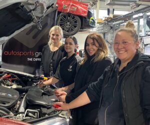 Group of women mechanics grouped around the engine of a car