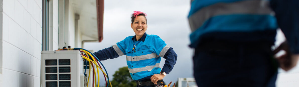 Woman HVAC technician standing on a roof in blue hi-vis